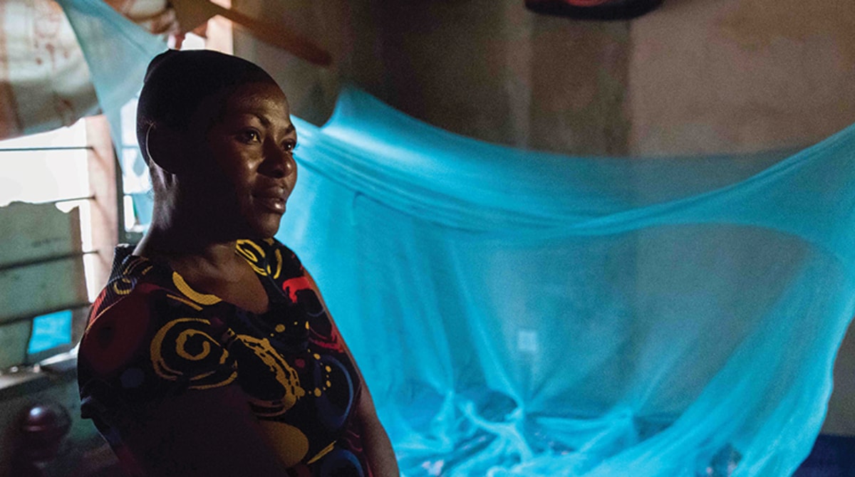 Woman stands in front of mosquito bed net used for malaria prevention in Tanzania