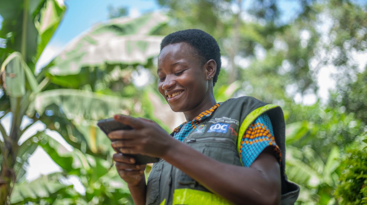 Woman wearing a CDC vest smiles as she holds electronic device.