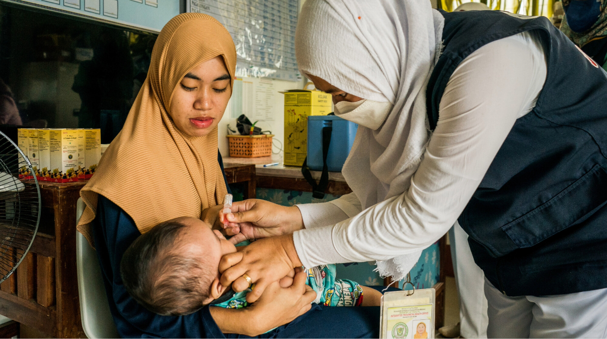 A healthcare worker administers oral polio vaccine drops to an infant held by its mother at a community health clinic.