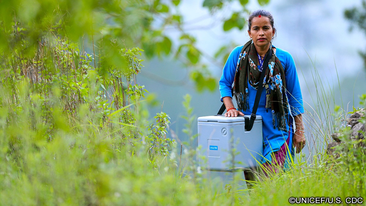 A health worker with a vaccine carrier en route to a community outreach session to vaccinate children.