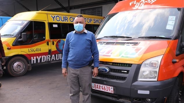 Khankhara wears a face mask and stands by two commuter buses outside of his garage.