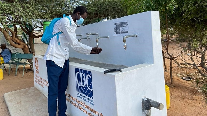 A person washes their hands at an outdoor handwashing station.