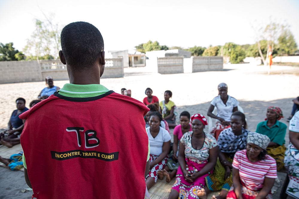 Man wearing red vest standing in front of seated group of people.
