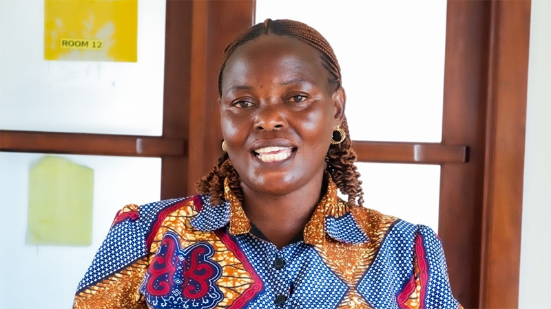 A woman wearing a colorful patterned blouse speaks during an interview in a bright indoor setting.