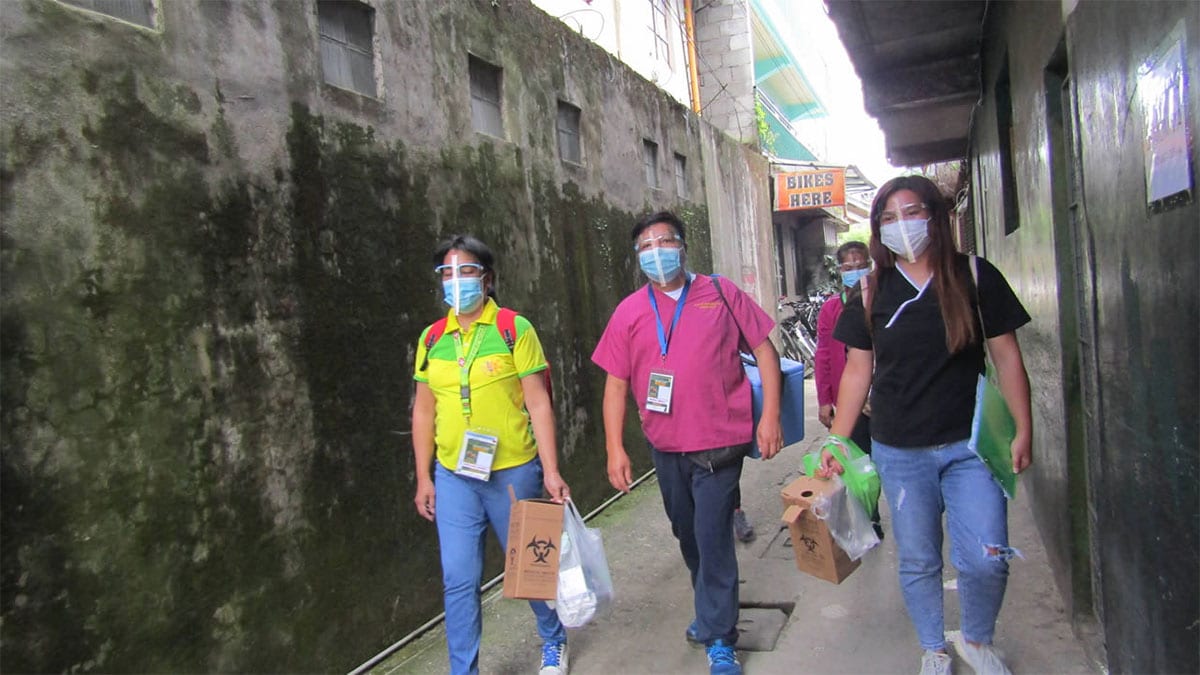 Masked health workers walk through narrow streets in the Philippines for a vaccination campaign.