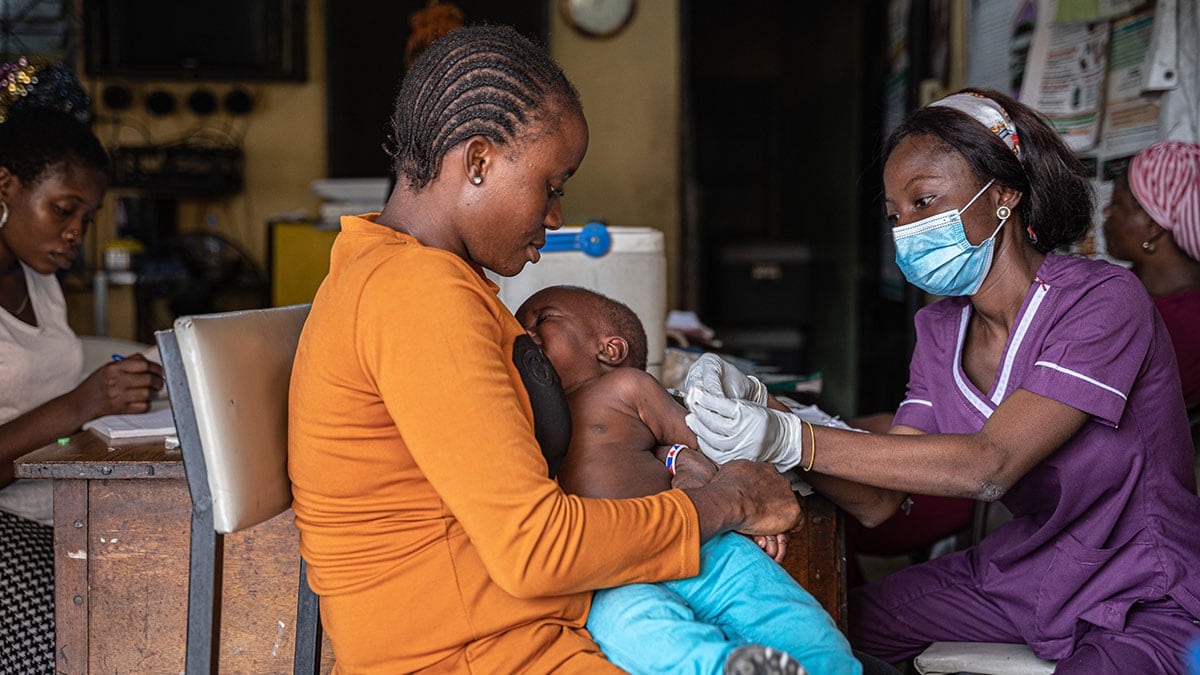 A mother holds her young son as a health worker gives a vaccine to the child.