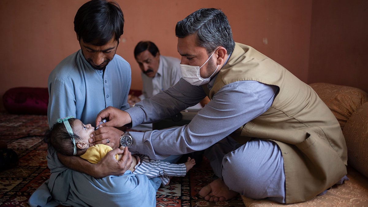 A health care worker administers oral polio vaccine to an infant being held by her father.