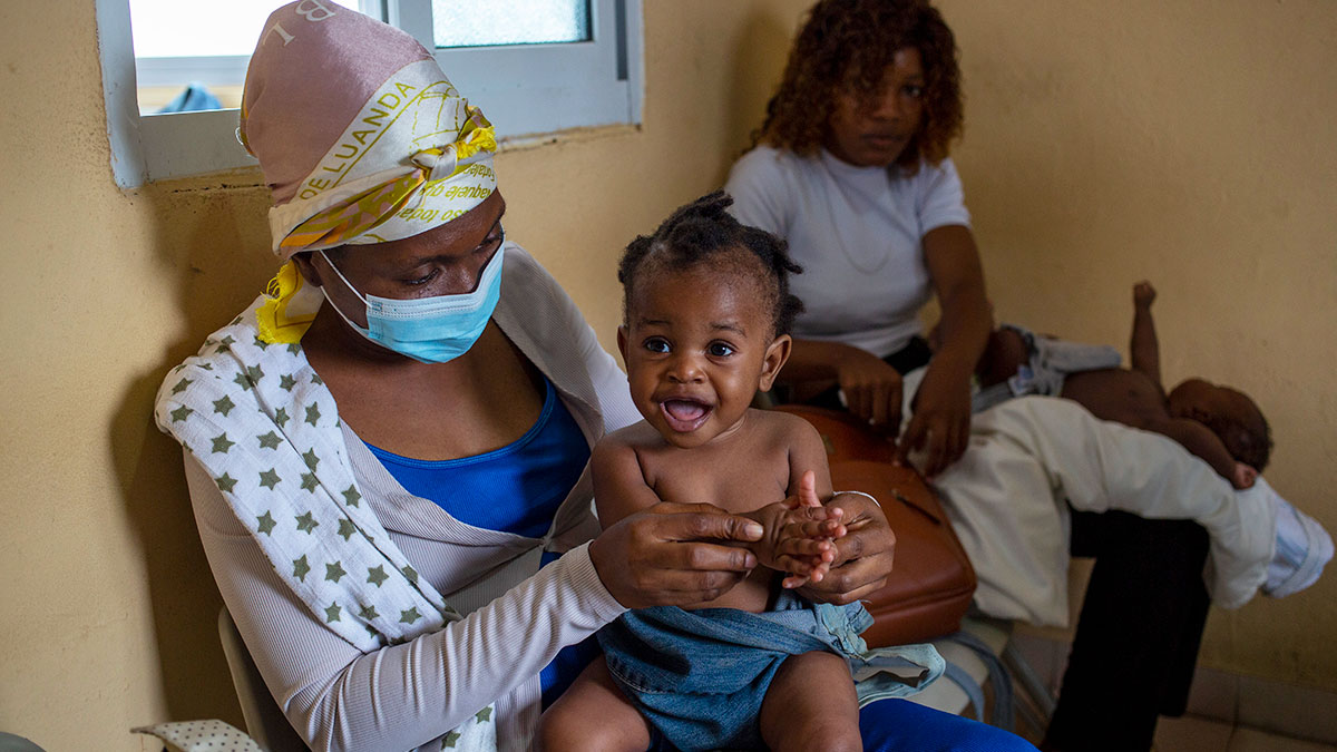 A mother holds her child in a health center as they wait for the child to receive a vaccine.