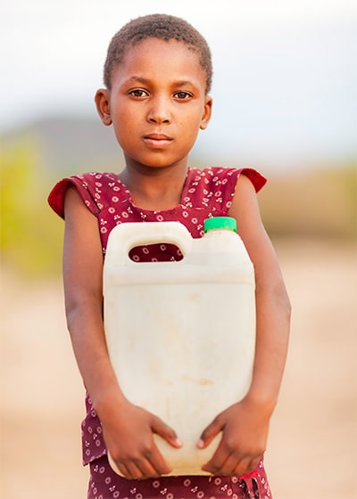 Child holding jug of water outside.