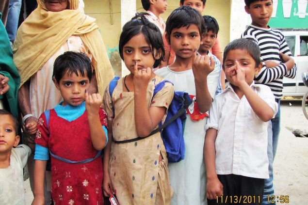 Children hold up their pinkie finger marked with indelible purple ink