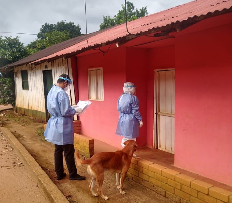 Two FETP residents conducting contact tracing in Mitu village, Vaupes, Colombia (border with Brazil) the first eleven COVID-19 cases were detected. A brown dog is near one of the residents.