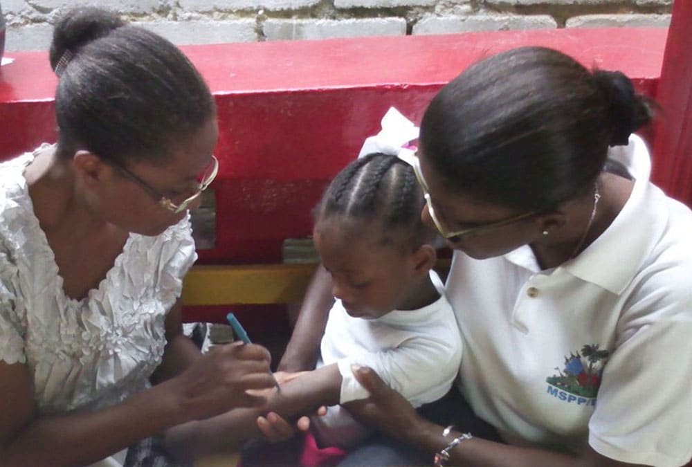 A nurse and an FETP Fellow draw a circle on a kindergartener's arm to measure body reaction to a tuberculosis test. Photo: Apollon Destinay Miracle and TEPHINET
