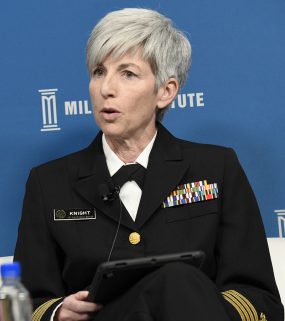CAPT Nancy Knight in uniform seated in chair speaking on stage with blue backdrop at the 2019 Milken Institute Global Conference