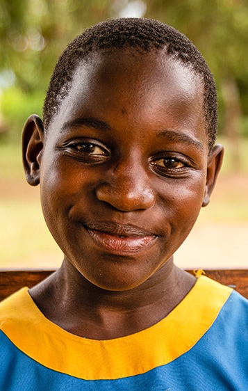 An 11-year old student from Luwero, Uganda, seated outside in front of her school.  Photo: RTI International