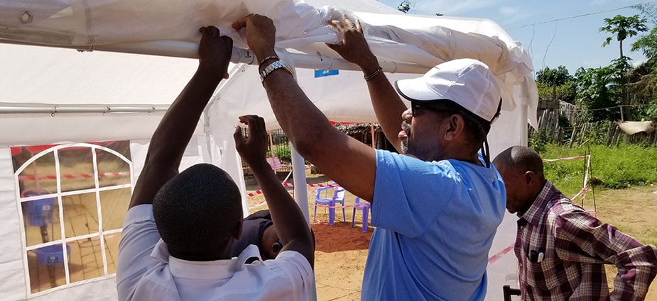 CDC’s Peter Thomas and a member of the Programme National pour l’Hygiene des Frontieres (PNHF) work to raise the sides of a screening tent in Kisangani City, DRC during a supervisory visit. Photo: Dante Bugli