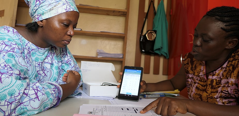 Local health worker demonstrating eIDSR to CDC's Fanny Koroma (in blue) during a field site visit. Photo: Julia Chen