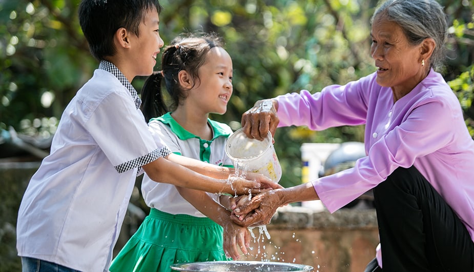 An elderly woman in Vietnam pouring water with one hand and using the other to help a boy and a girl wash their hands. Photo: Scott McPherson, RTI International