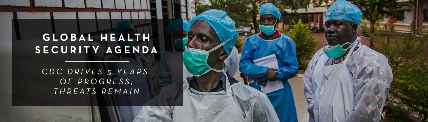 Global Health Security Agenda: CDC Drives 5 Years of Progress; Threats Remain. Local healthcare workers in Guinea wearing face masks and medical gear with a man in front of the group writing on a paper chart.
