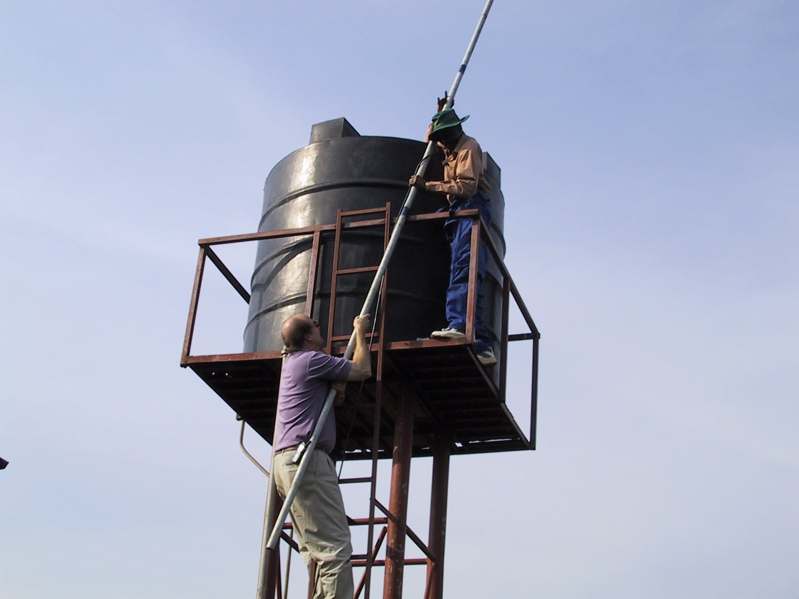 Alt Text: Two men on top of a tower installing an antenna