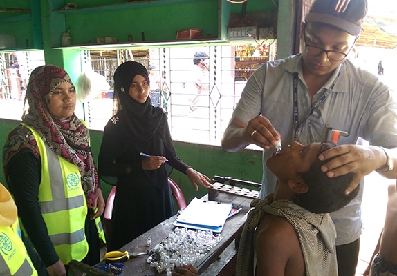 Dr. Mostafa Moin Uddin, IMPACT-Bangladesh graduate, delivering oral cholera vaccine to a Rohingya child in the Cox Bazar refugee camp helps to prevent the spread of this dangerous disease. Photo: Dr. Nurullah Awal, IMPACT-Bangladesh