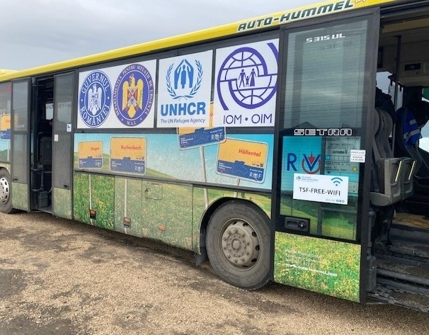 Bus with logos from UNHCR, IOM, & Romanian Government transporting displaced Ukrainians from Moldova-Ukraine border to Romania.