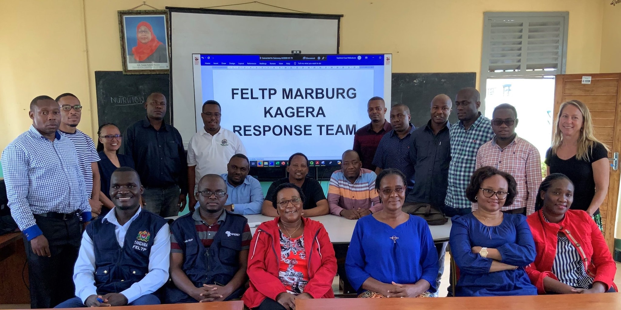 Group of people sitting at a table in front of a slide that says FELTP Marburg Kagera Response Team