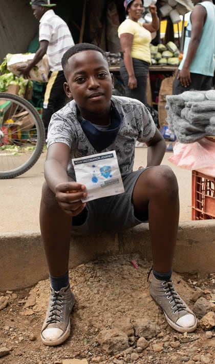 A boy proudly displays his vaccination record card while sitting curbside on a street in South Africa.