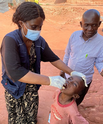 A healthcare worker vaccinates a child using oral drops while an adult looks on in Democratic Republic of the Congo, 2021.