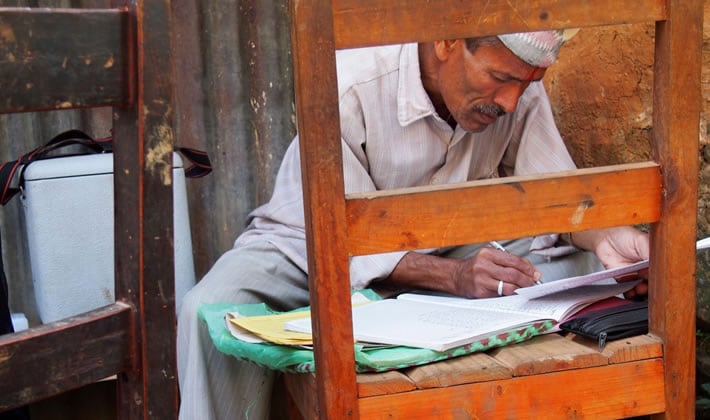 Polio health care worker uses a chair as both seat and desk as he records data in the field.