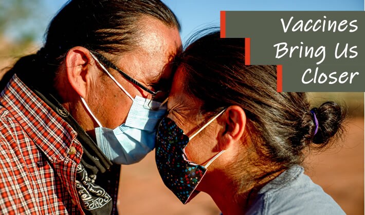 Vaccines bring us closer. Two Ute Native Americans wearing face masks lean close to each other, smiling.
