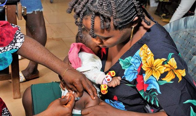 Woman holds infant receiving a vaccine in Nigeria, 2021.