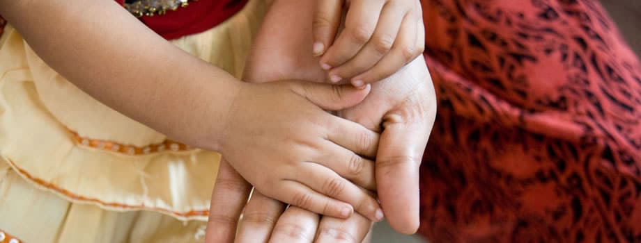 A young girl's hand rests in the hand of her mother.
