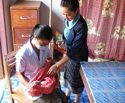 Woman holds newborn receiving a vaccine by a healthcare worker at a clinic in Lao-PDR.