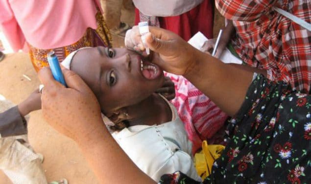 Uma criança inclina a cabeça para receber a vacina oral contra a poliomielite na Nigéria.