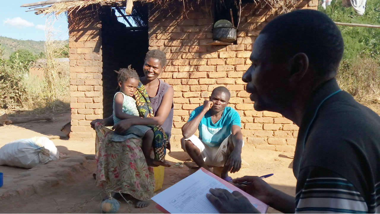 Public health worker interviews a family outside their mud brick home in Malawi.