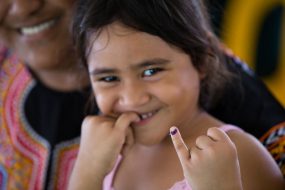 A young girl holds up her pinky finger, which is marked to show she has received her measles vaccination.