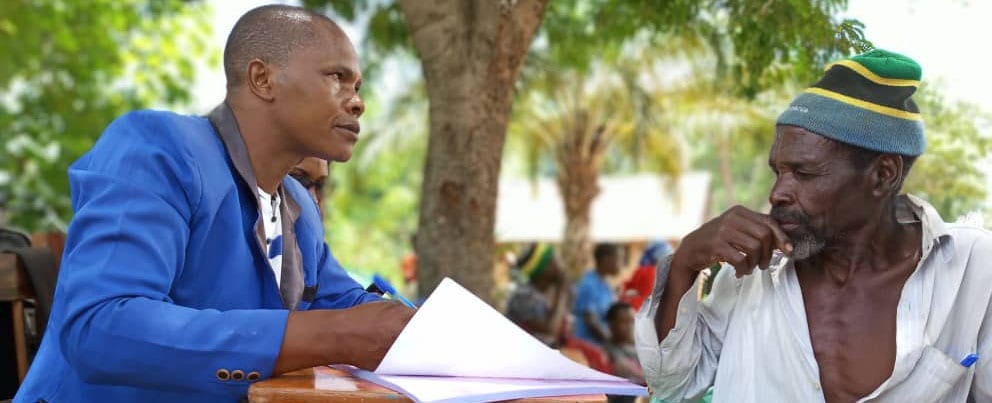 Health worker and patient sit outdoors at a table in an HIV/TB clinic in Tanzania
