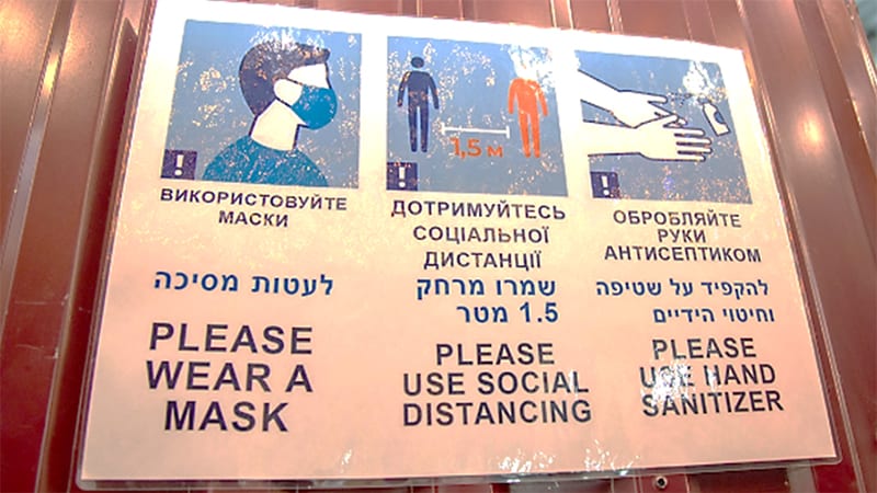 This poster hangs in a large dining hall set up by Rabbi Zvi Gluck’s organization, <a href="https://amudim.org/about-amudim/">Amudim</a>. The poster has images of three things to do to lower the risk of getting COVID-19. Below each image, the action is spelled out in Ukrainian, Hebrew, and English: “please wear a mask,” “please use social distancing,” and “please use hand sanitizer.” Photo by Svitlana Kravchenko, US embassy in Ukraine 

