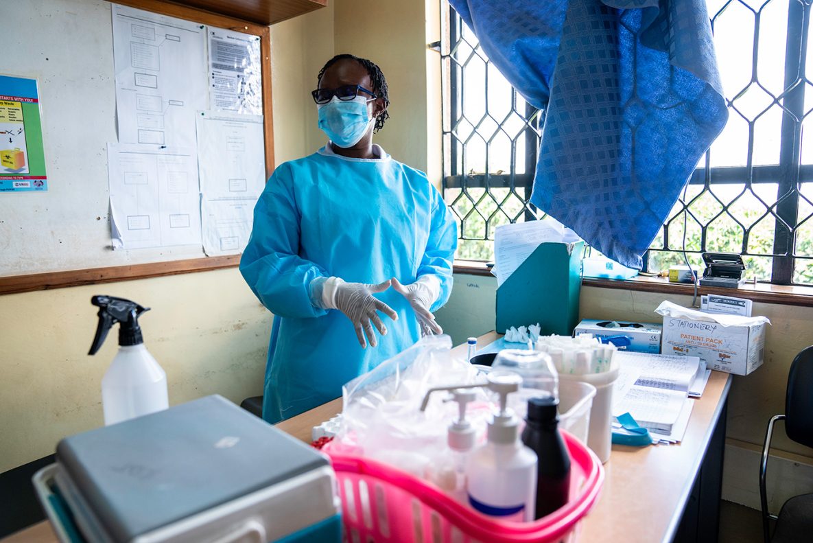 Healthcare worker standing near a table talking about Kenya’s vaccination plan at a free clinic that serves the community.