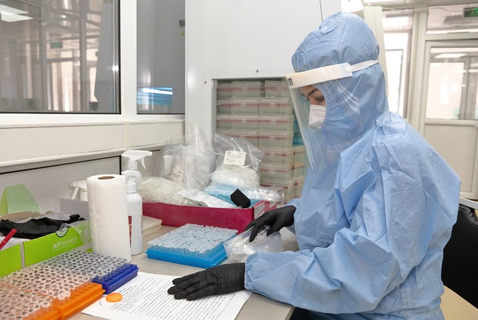 Photo of a laboratory technician wearing protective clothing who is registering samples and checking them for quality as part of the process for running a COVID-19 PCR test.