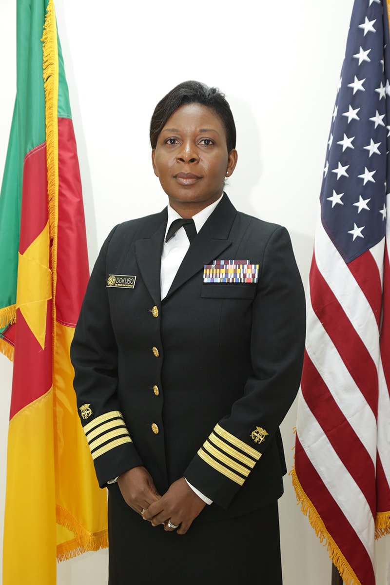 Photo of CDC Cameroon Country Director Dr. Emily Kainne Dokubo standing in front of flags for Cameroon and the United States.