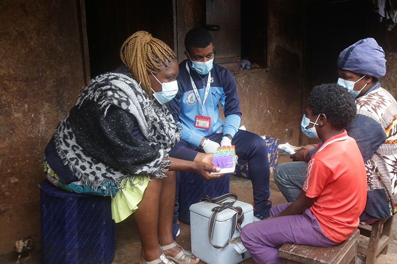 Photo of healthcare workers with a medicine container sitting across from two people outside a home.