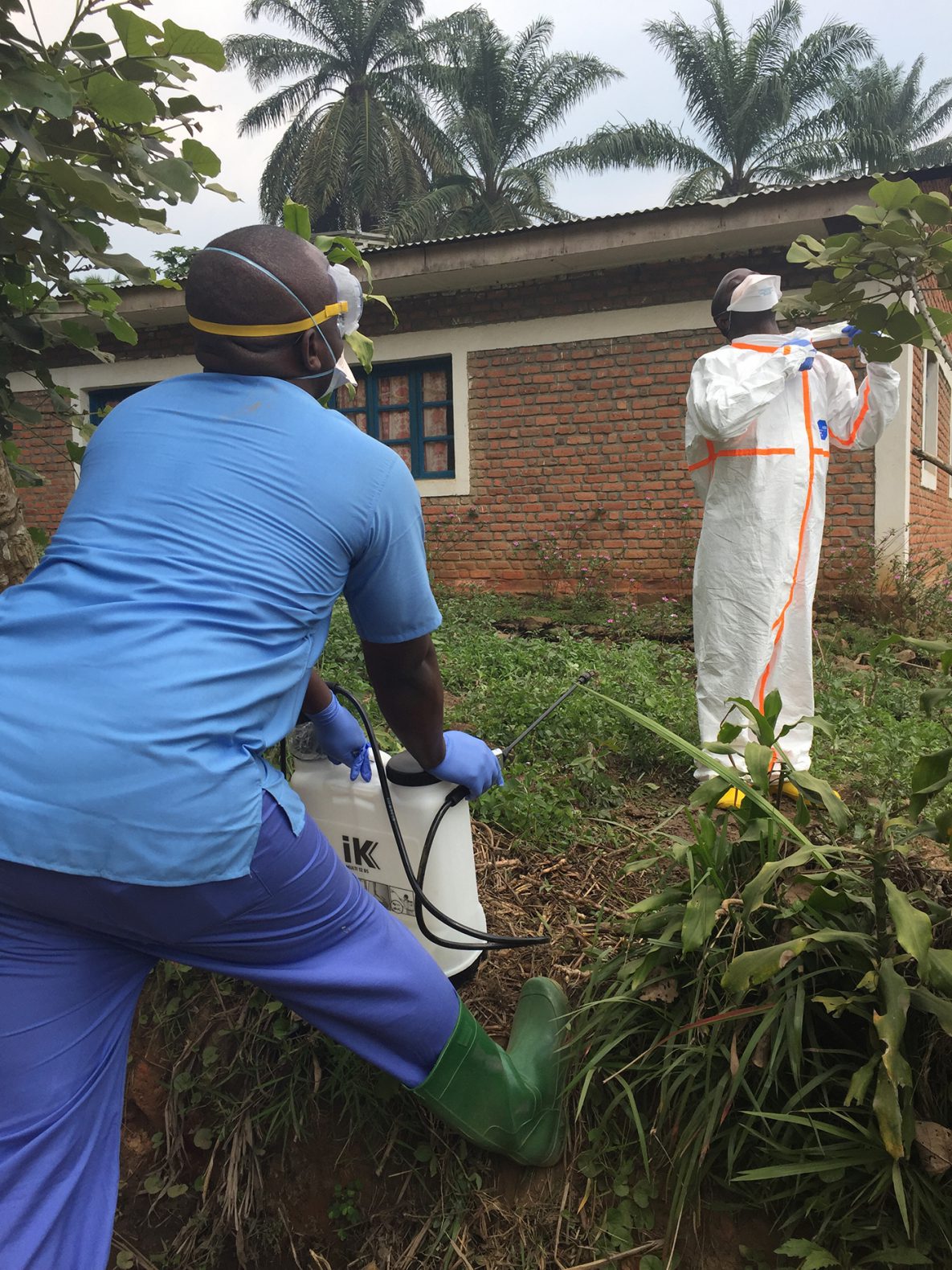 A new set of Ebola cases in South Kivu posed additional challenges for responders due to the distance to an Ebola Treatment Center. The Local Health Center (Centre de santé de Chowe) was turned into a makeshift transit center until an Ebola Treatment Center could be built down the road. Pictured is a healthcare worker removing personal protective equipment (PPE) with supervision from a colleague using a hedge to mark the edge of the contaminated area—the hot zone.