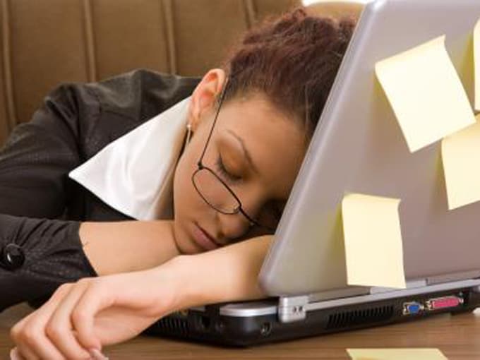 a woman sleeping at work, with her head and arms over a laptop keyboard
