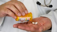 A healthcare provider holds a pill bottle and two white pills.