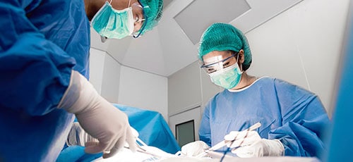 Un médico y una enfermera con instrumentos quirúrgicos en las manos haciendo una operación, en una sala operatoria.