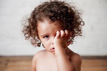 Una niña pequeña se frota el ojo izquierdo