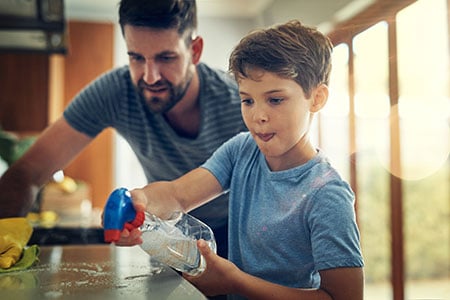 Father and son clean counter tops with spray bottle and cloth