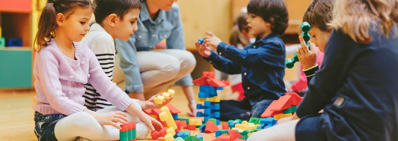 Children sitting on classroom floor playing with blocks.