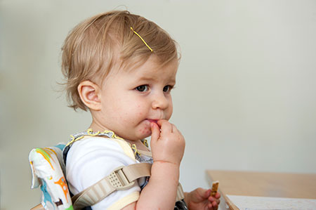 Toddler girl with red spots around the mouth, eating at a table.